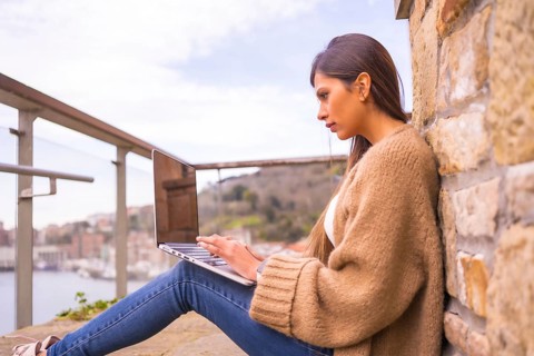 A young Latin woman in a white t-shirt and a brown wool sweater working on the terrace of her house