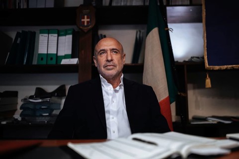 A confident business executive in formal attire sits at a desk in an office. The setting includes