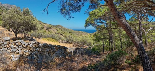 Stone wall in a hilly landscape on the hiking trail from Avlona to Diafani with a view of the sea,
