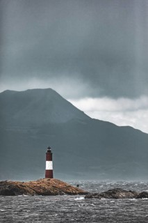 Lighthouse in a storm on a lonely rocky island in front of a mountain range, The lighthouse in the