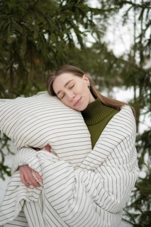 A serene scene showcasing a woman wrapped in a cozy striped blanket, embracing a pillow amidst