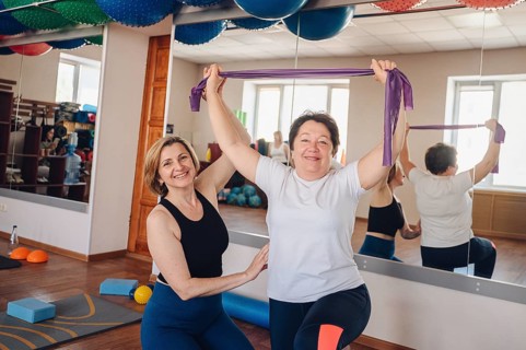 Woman in a gym participate in a fitness class with a female instructor, using resistance bands for