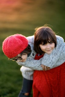 A young boy and girl, siblings, playfully embrace in a fall sunset. The boy wears glasses and a red