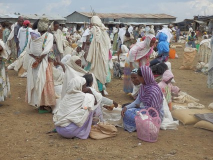 A lively market with lots of people in traditional clothes standing and interacting in groups,
