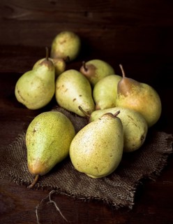 A collection of ripe pears arranged on burlap, set against a dark wooden surface. The lighting