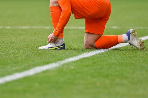 The football player ties shoelaces in his shoe on the turf of the pitch in Lubin, Poland
