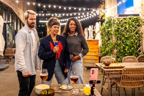 Multi-ethnic male and females friends singing karaoke after dinner in the terrace of a night bar