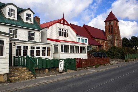 Row of houses with different roof colours on a quiet street next to a brick church, Stanley, East