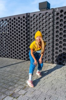 Smiling young woman wearing a yellow beanie and blue overalls dancing an urban choreography in the