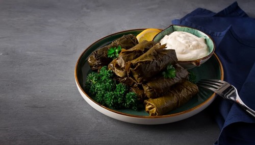 Dolma, cabbage rolls, grape leaves with filling, white sauce, lemon and herbs, rustic, selective