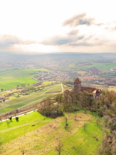 An old castle in the middle of a green landscape with a wide view of a village and fields under a