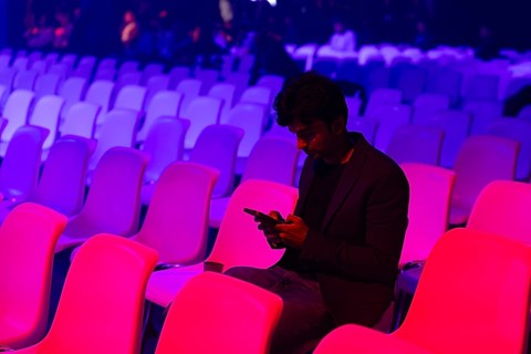 A indian man sits alone in an auditorium filled at a conference of AI in Amsterdam with colorful