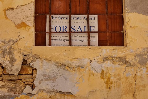 Shop sign behind a window with a weathered yellow façade and crumbling plaster, Symi Town, Symi,