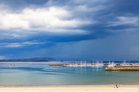 Seascape view at a marina with boats at a pier and a sand beach and a dark storm clouds on the sky,
