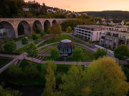 Aerial view of a wooden ball in the park, surrounded by trees and near an aqueduct at sunset,