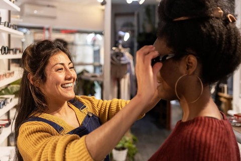 A cheerful shop assistant helps a customer try on a pair of stylish sunglasses in a cozy boutique.