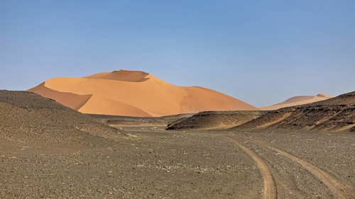 Vast desert landscape with sand dunes and tracks under a clear sky, The endless sand dunes of the