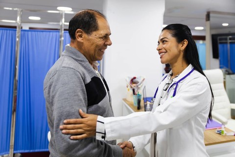 A smiling young female doctor provides attentive care to an elderly male patient in a Latin