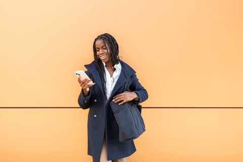 A young cheerful African American businesswoman with braids checks her smartphone, dressed in