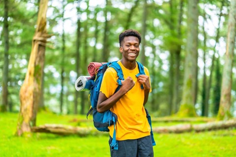 Portrait of a cheerful young african man hiking through green forest