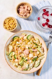 A fresh salad featuring tuna, corn, and cucumber on a striped cloth. Complemented by a drink with