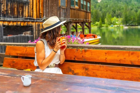 Young woman relaxing with a mug by lake dobbiaco, enjoying the peaceful mountain view in the