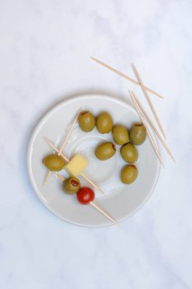 Stuffed olives on plate with cheese cubes and tomato, toothpick