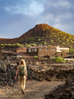 A woman with a backpack traverses the stark, volcanic terrain of Timanfaya National Park in