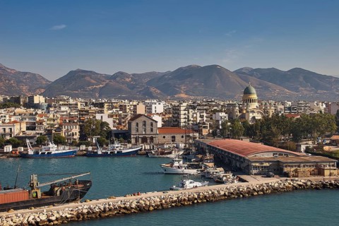 Coastal town with port and ships, surrounded by mountainous landscape, old ferry port in the center