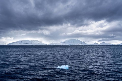 Drifting ice in the dark, moving Southern Ocean against snow-capped mountains under cloudy sky,