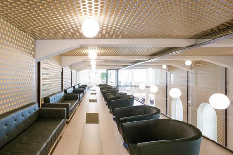 A contemporary lounge in club features stylish seating and a distinctive perforated ceiling design.