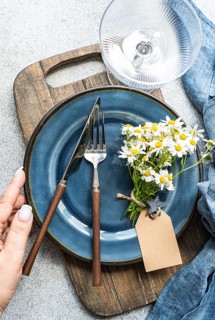Top view of cropped unrecognizable hands of a woman adjust cutlery on a blue plate with summer