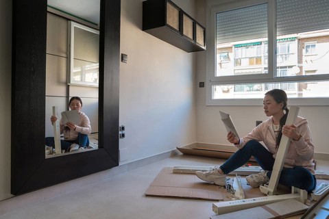 Young Asian woman assembling a white desk at home, focusing intently on the instruction manual. DIY