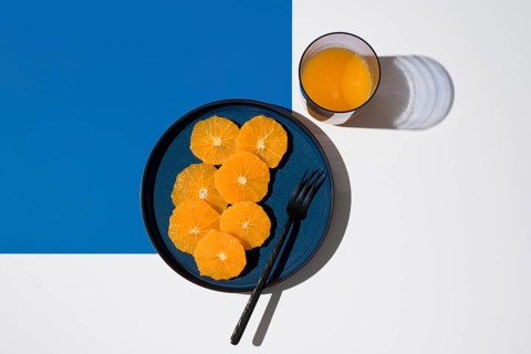 Bright and fresh, sliced oranges are artfully arranged on a blue plate beside a glass of orange