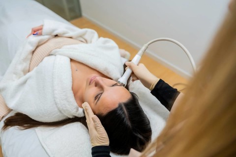 Woman in bathrobe receiving a professional facial skin care treatment with a specialized device