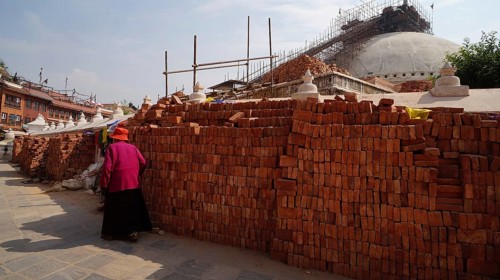 Rebuilding Bodnath after the earthquake, a woman wearing traditional clothes walks past bricks and