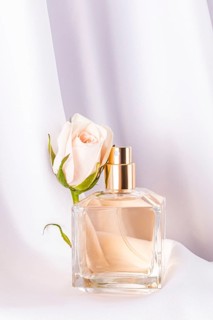 A delicate rose blossom complements an elegant perfume bottle, set gracefully on soft white fabric.