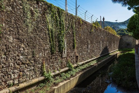 Old stone wall topped with barb wire fence and ditch filled with water, La Spezia Naval Base, La