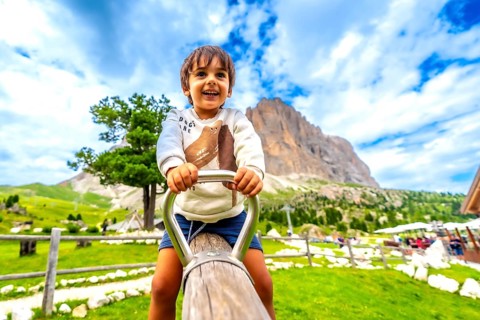 Happy child playing on a swing in a playground in the italian dolomites mountains, with the