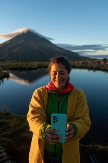 Smiling woman takes a selfie with a smartphone during sunrise at Mount Taranaki, Nueva Zelanda. The