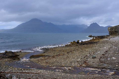 View of a cloud-covered coastal landscape with mountains and pebble beach by the sea, Elgol Beach,