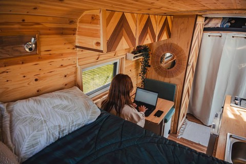 A woman works remotely on her laptop in a beautifully designed camper van with wooden interiors.