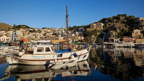 Fishing boat in a quiet harbour with reflecting buildings. Mediterranean surroundings in clear