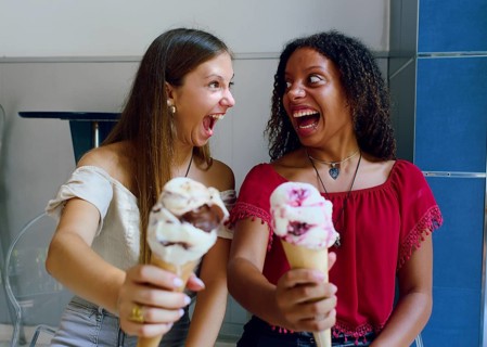 Two teenage girls, one Caucasian and one African descent, laughing joyfully while holding ice cream