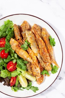 Fried crispy mullet fish, with fresh salad, on a plate with lime, no people