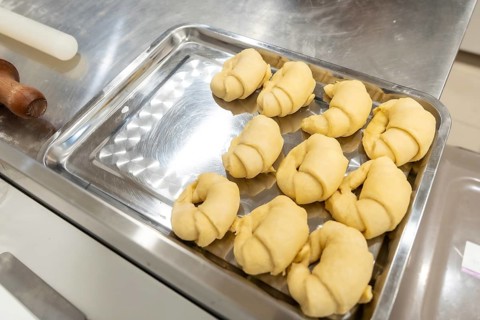 Raw crescent rolls dough arranged on a metal baking tray, preparing for baking in a commercial