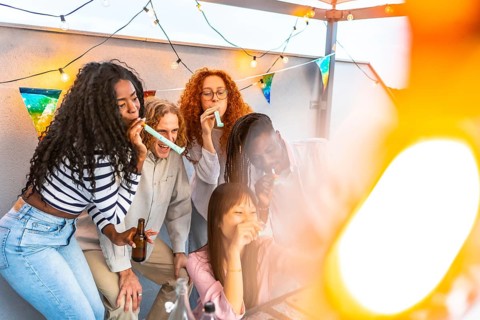 Multiracial millennial friends blowing streamers while taking selfie during birthday party at
