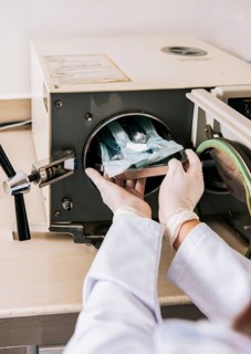 Close up of hands with dental autoclave sterilizer machine. Dentist hands sterilizing tools with
