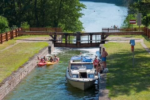 A boat and canoes travelling on a river through the lock, surrounded by green nature, Sluza