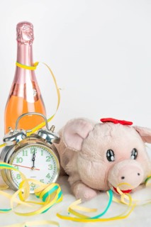 Plush pig, champagne bottle and alarm clock with colourful streamers on a white surface, New Year's